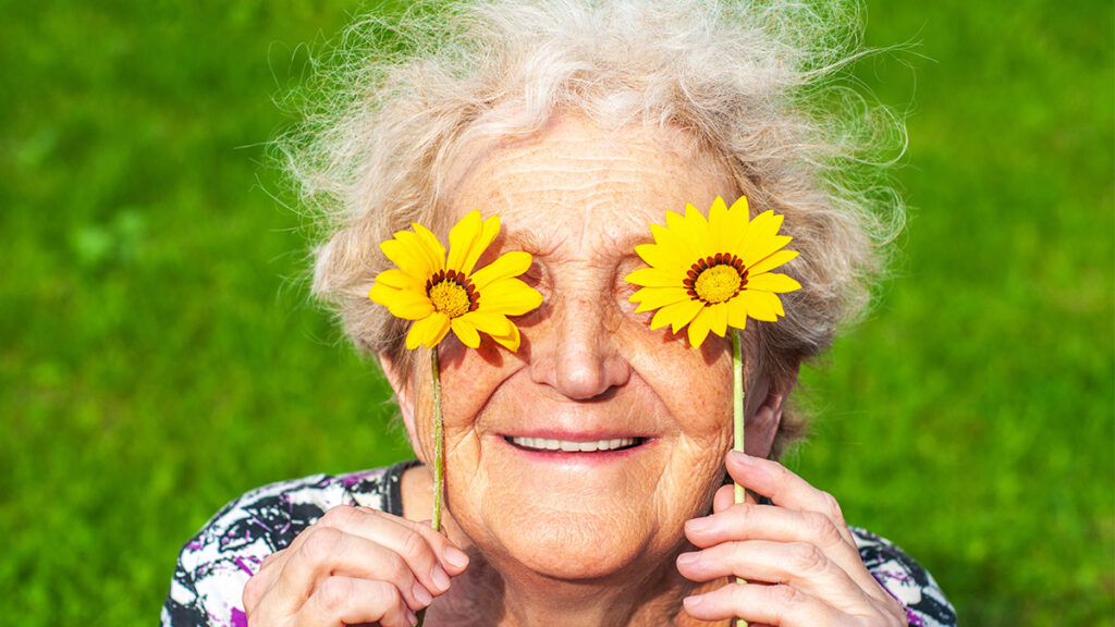 Elderly woman in the sun holding up flowers to her eyes