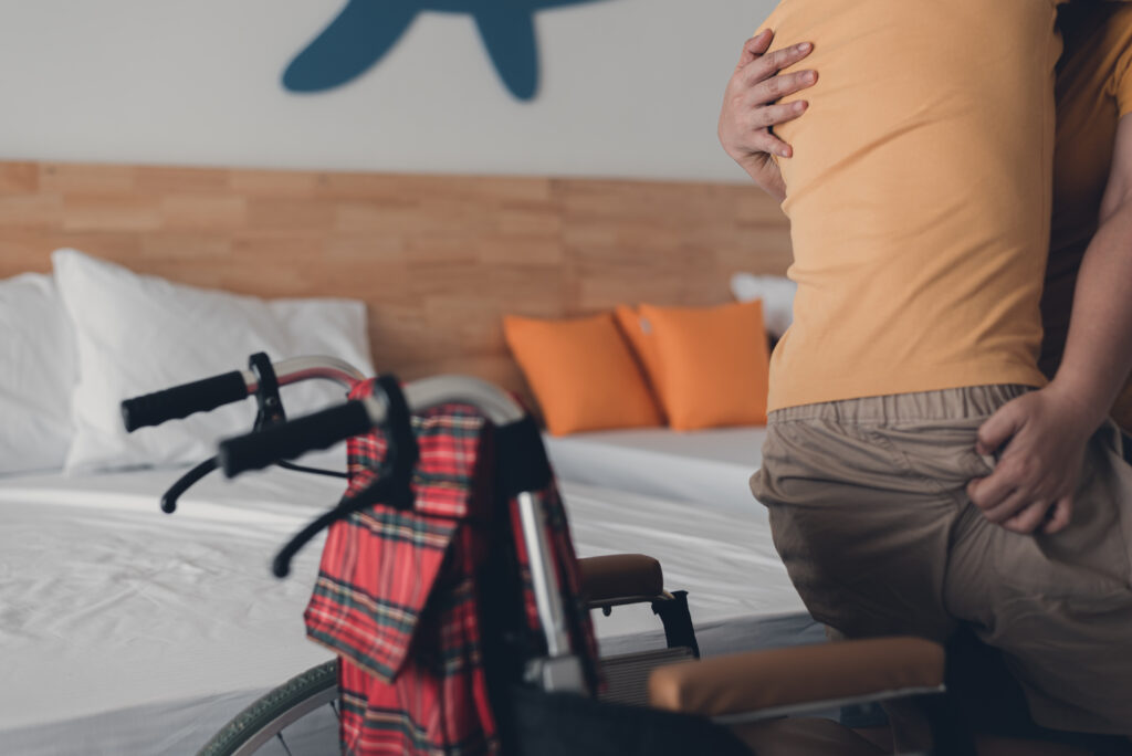 Parent helping handicapped teenager boy move from bed to wheelchair